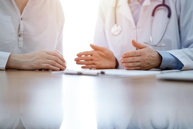 Doctor and patient discussing something while sitting near each other at the wooden desk in clinic. Medicine concept