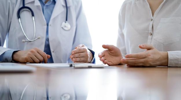 医師と患者は診療所の木製の机に近くに座りながら何かについて話し合っています。医学の概念。