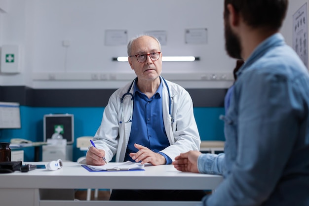 Врач и пациент обсуждают диагноз при осмотре в кабинете. Специалист в области здравоохранения объясняет лечение и медицинскую поддержку мужчине после консультации с врачом.