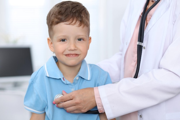 Foto medico e paziente in ospedale ragazzino felice che si diverte mentre viene esaminato con lo stetoscopio concetto di assistenza sanitaria e assicurativa