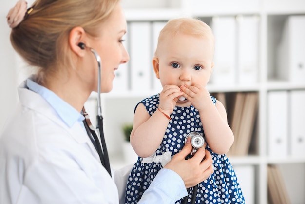 Doctor and patient in hospital. Little girl dressed in dark blue dress is being examined by doctor with stethoscope. Medicine and healthcare concept.