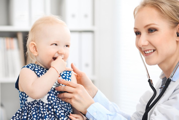 Doctor and patient in hospital. Little girl dressed in dark blue dress is being examined by doctor with stethoscope. Medicine and healthcare concept.