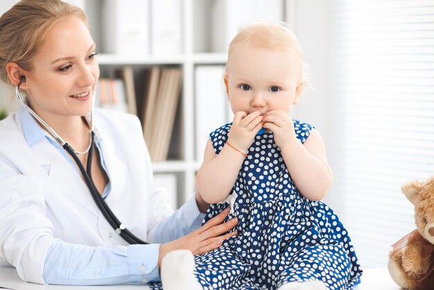 Doctor and patient in hospital. Little girl dressed in dark blue dress is being examined by doctor with stethoscope. Medicine and healthcare concept.