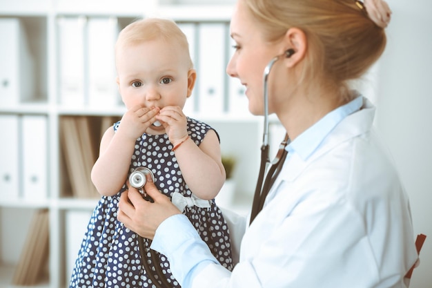 Doctor and patient in hospital. Little girl dressed in dark blue dress in peas is being examined by doctor with stethoscope. Medicine concept.