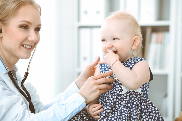 Doctor and patient in hospital. Little girl dressed in dark blue dress in peas is being examined by doctor with stethoscope. Medicine concept.