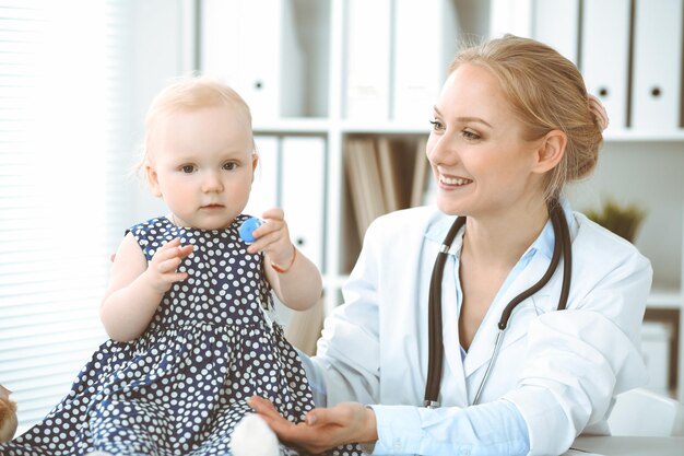 Doctor and patient in hospital. Little girl dressed in dark blue dress in peas is being examined by doctor with stethoscope. Medicine concept.