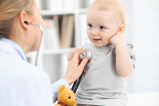 Doctor and patient in hospital. Little girl dressed in grey dress is being examined by doctor with stethoscope. Medicine concept.