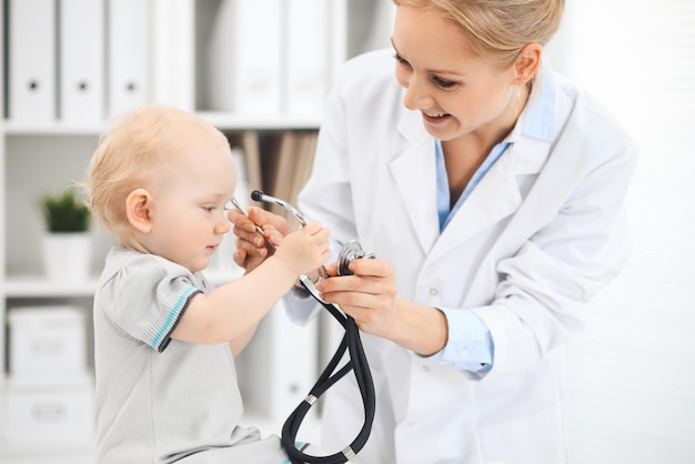 Doctor and patient in hospital. Little girl dressed in grey dress is being examined by doctor with stethoscope. Medicine concept.