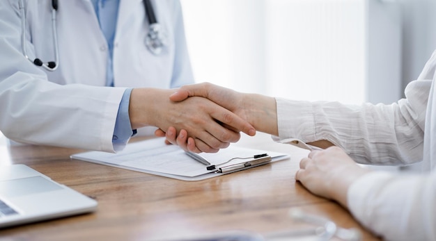 Doctor and patient shaking hands above the wooden table in clinic. Medicine concept.