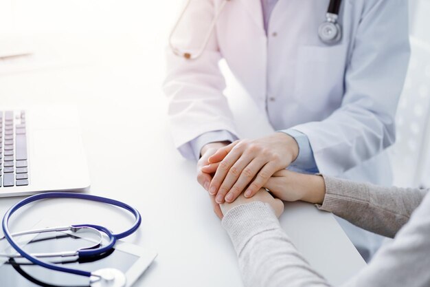 Photo doctor and patient sitting at the table in clinic office. the focus is on female physician's hands reassuring woman, only hands close up. medicine concept
