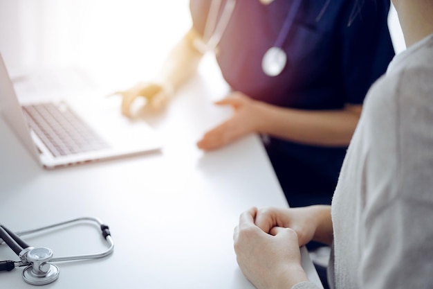 Doctor and patient talking to each other during current health examination while sitting at the desk in clinic, closeup of hand. Perfect medical service and medicine concept.