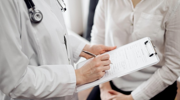 Doctor and patient view. Female physician is filling up a medical records form near a woman having a medical examination. Medicine concept.