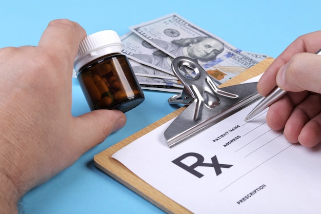 Врач или фармацевт, держа в руке банку или бутылку таблеток на фоне банкнот долларов и писать рецепт на специальной форме. медицинские расходы и концепция оплаты здравоохранения.