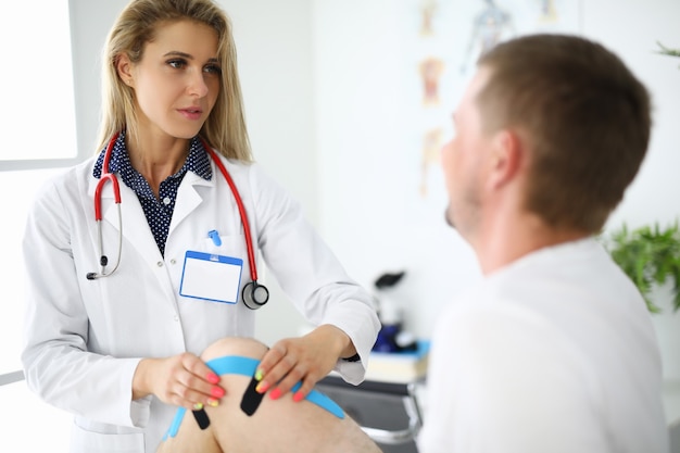 Doctor physiotherapist sticking tapes on man sore knee