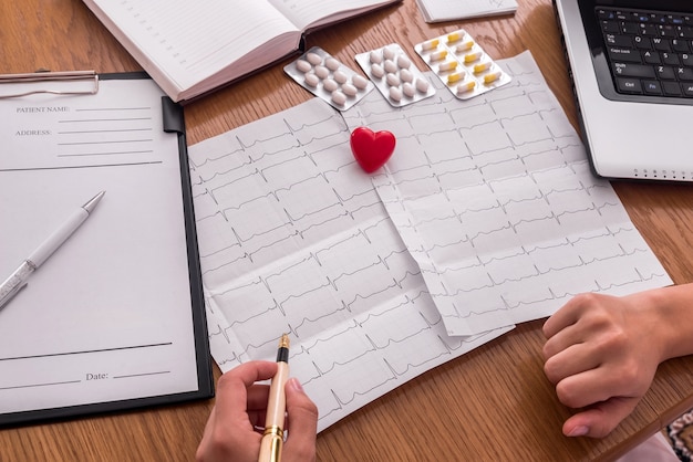 Doctor pointing on patient's cardiogram, pills and red heart