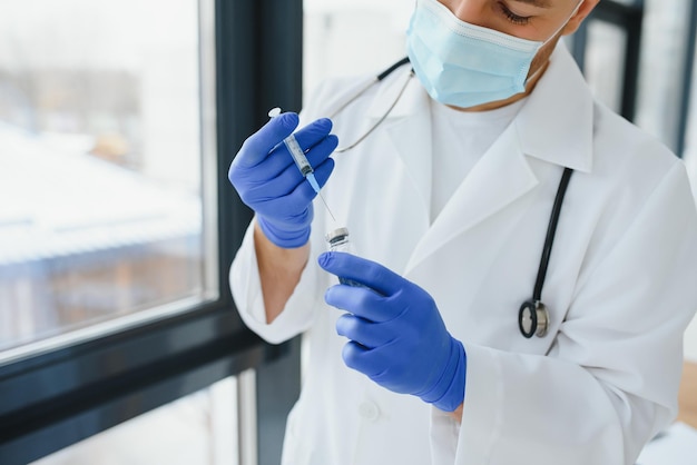 Doctor in PPE holding a vial or bottle vaccine against coronavirus Covid 19 new Omicron variant or strain in his hand, close up. Concept of vaccination, trial and treatment due to SARS-CoV-2 pandemic