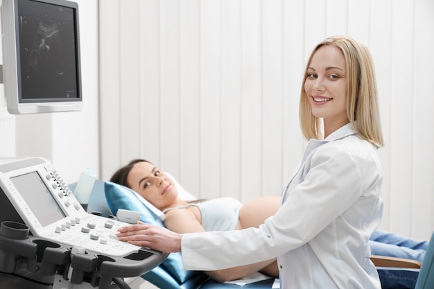 Medico e donna incinta che sorridono, posando in gabinetto medico