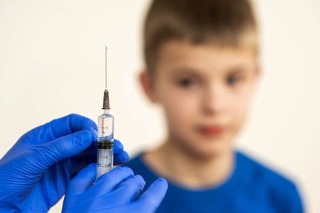 Doctor preparing vaccination injection with a syringe to an afraid child boy. Vaccination of children at school concept.