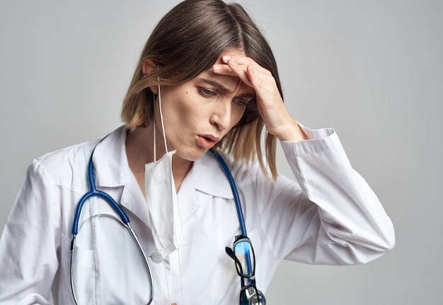 Doctor professional with a stethoscope and in a medical gown on a light background medical mask