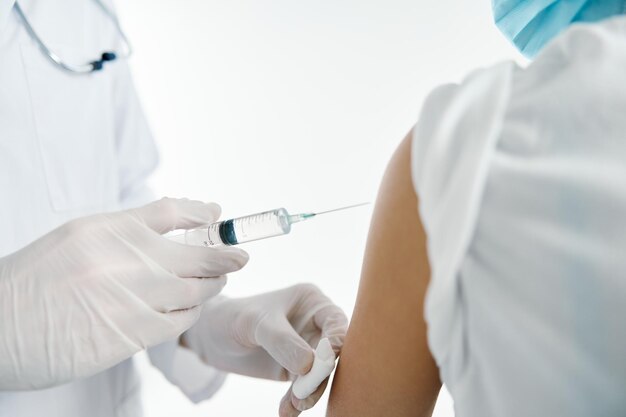 Doctor in protective gloves injects a vaccine into the shoulder\
of a woman patient in a hospital covid