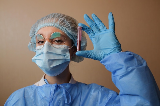 A doctor in a protective mask and glasses holds a test tube with a positive blood test for COVID19