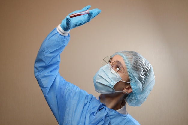 A doctor in a protective mask and glasses holds a test tube with a positive blood test for COVID19