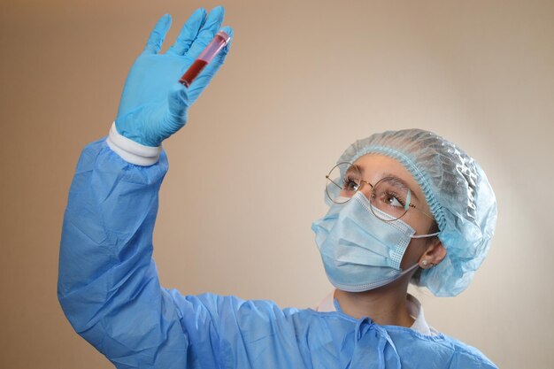 A doctor in a protective mask and glasses holds a test tube with a positive blood test for COVID19