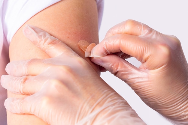 보호용 의료용 장갑을 낀 의사가 백신을 주사한 후 여성의 팔에 접착 붕대를 감고 있습니다.