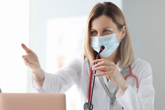 Doctor in protective medical mask speaking into microphone. Presentation at conference concept