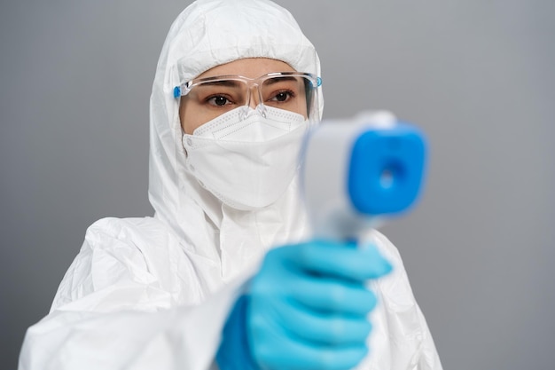 Doctor in protective PPE suit scanning with infrared thermometer, IR Thermoscan