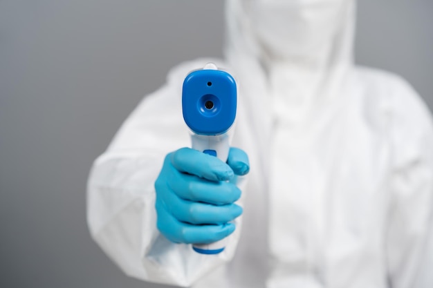 Doctor in protective PPE suit scanning with infrared thermometer, IR Thermoscan