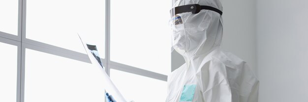 Doctor in protective suit holding X-ray photograph in clinics office