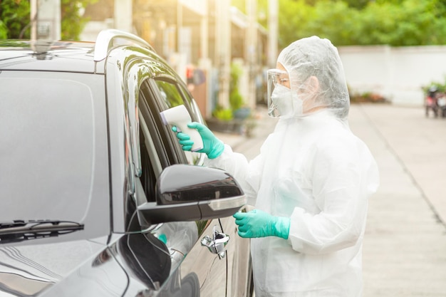 Doctor in protective suit PPE holding test kit. Medical worker performing drive-thru Covid-19 test, taking nasal swab sample patient through car window, PCR diagnostic, Rapid antigen test kit (ATK)