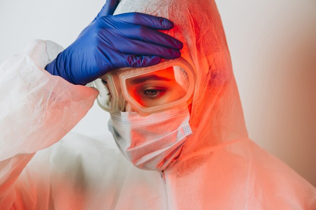 Doctor in protective uniform, glasses, gloves on a blue background in neon light. close-up portrait of a doctor in red neon. tired man is battling a coronavirus. COVID 19