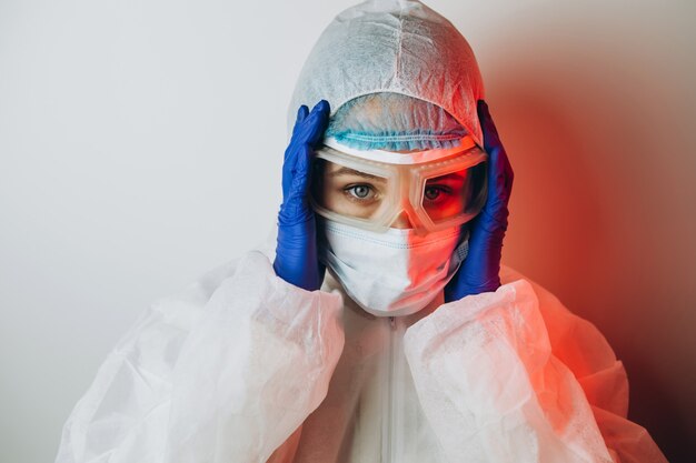 Doctor in protective uniform, glasses, gloves on a blue background in neon light. close-up portrait of a doctor in red neon. tired man is battling a coronavirus. COVID 19