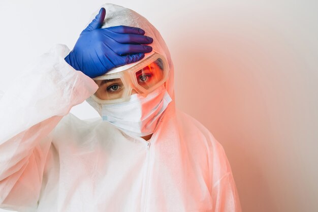 Doctor in protective uniform, reperitor, glasses, gloves on a blue wall in neon light. A close-up portrait of a doctor in red neon. A tired man is battling a coronavirus. COVID 19