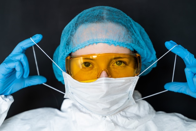 의사는 검정색 배경에 마스크를 넣습니다. 새로운 코로나 바이러스의 유행성 개념