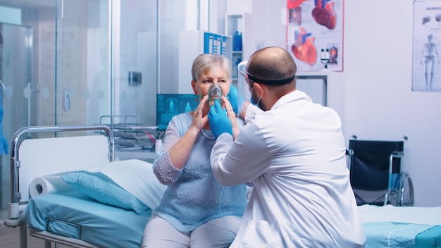 의사는 현대적인 사설 병원이나 진료소에서 COVID-19 코로나바이러스가 발생하는 동안 은퇴한 노년 여성에게 산소 마스크를 씌웠습니다. 감염 및 질병 퇴치 및 검역