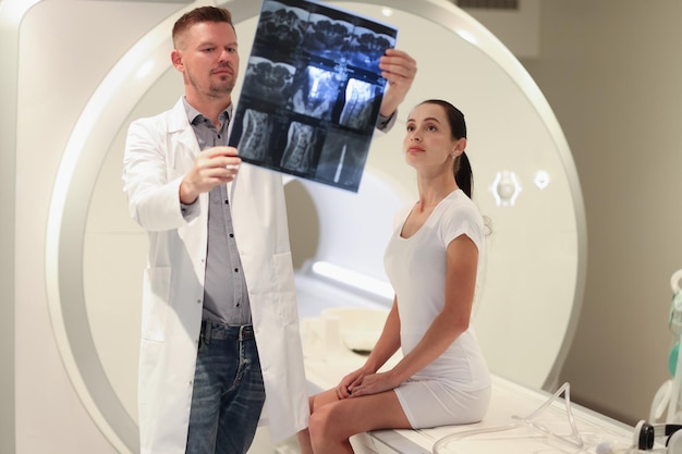 Doctor radiologist looking at snapshot of patient spine in front of mri machine spinal hernia