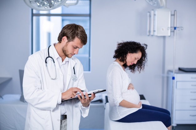 妊娠中の女性を調べながら医師がクリップボードを読む