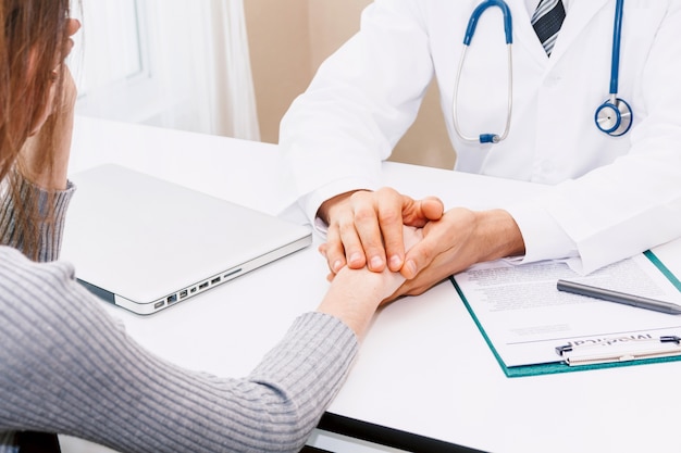 Doctor reassuring her female patient with care on doctors table in hospital