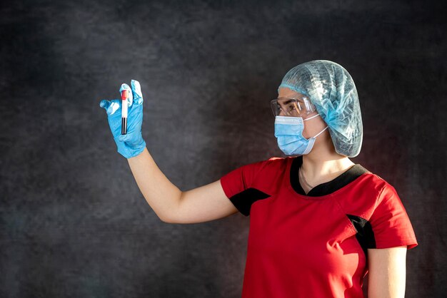 Doctor in red uniform and protective cloth holding test tube with blood sample for analysis COVID19 Medical test tubes