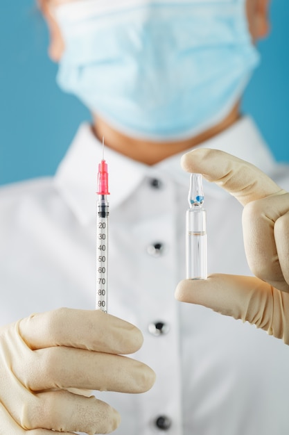 A doctor in rubber gloves holds an ampoule of medicine and a syringe, close-up. Medicine for flu, measles, coronavirus, Covind-19 vaccine disease.