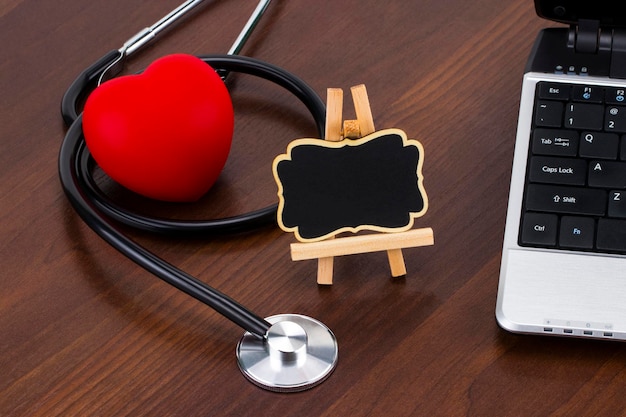 the doctor's desk with laptop, stethoscope and red heart and blackboard with empty space for a text.