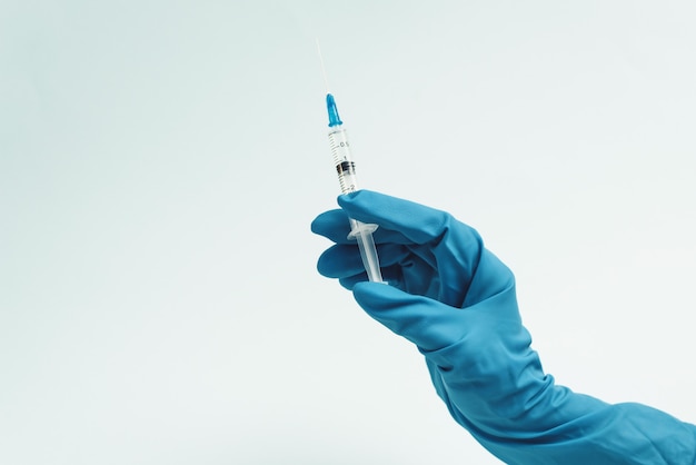 Doctor's hand in a blue rubber glove holds a medical syringe on a blue background. The concept of medicine and medical care for the patient