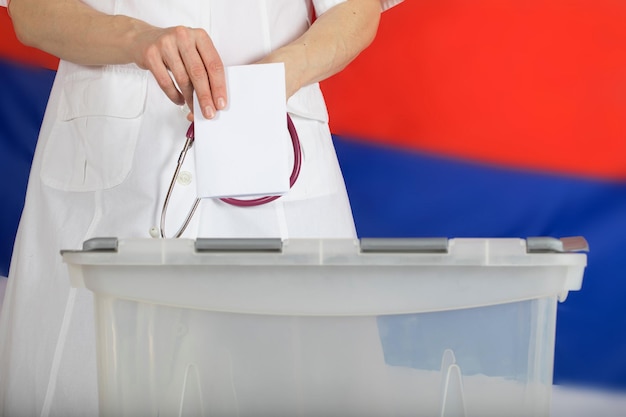 Photo doctor's hand casts ballot paper in the ballot box. russian flag in the background.