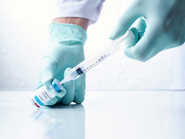 A doctor's hand extracting the Covid-19 vaccine from a vial, white background.