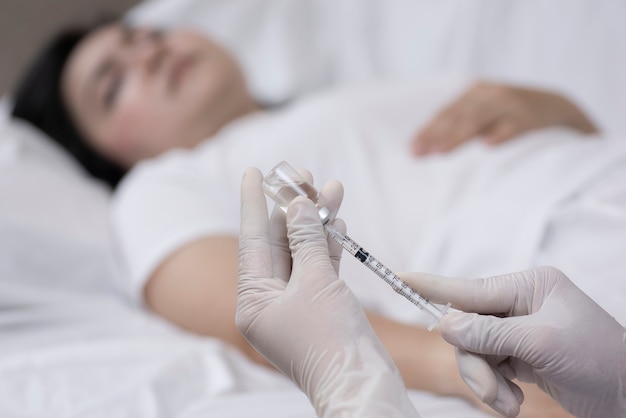 Doctor's hand holding draw syringe with vial for injection into female patient on bed in Emergency room