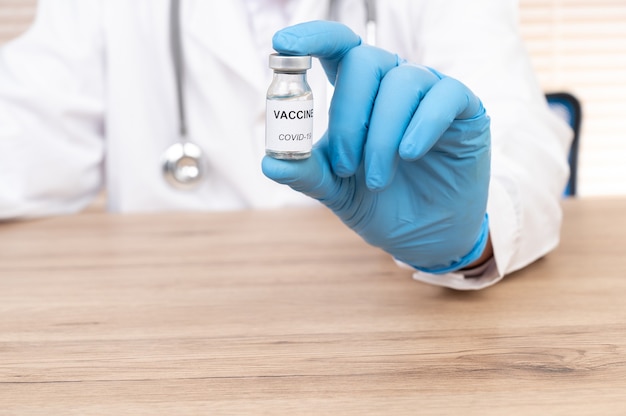 Doctor's hand holding vaccine vial on the doctor's desk