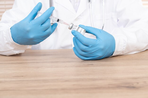 Рука врача, держащая флакон с вакциной и шприц с covid-19 на столе врача